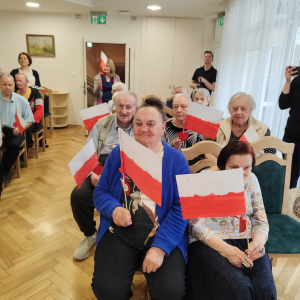Na zdjęciu widać Mieszkańców Domu Pomocy Społecznej Pracownika Oświaty wraz z otrzymanymi, ręcznie malowanymi flagami podarowanymi przez Dzieci z Przedszkola nr 42 w Warszawie.