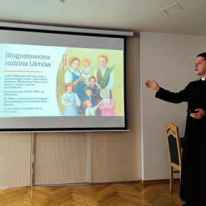 Kleryk Hubert opowiada o rodzinie Ulmów. Na rzutniku widac grafikę rodziny.
